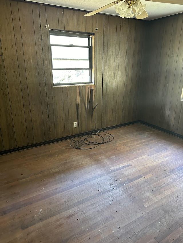 unfurnished room featuring wood walls, a ceiling fan, and hardwood / wood-style flooring