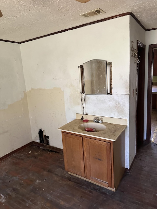 bathroom with vanity, a textured ceiling, visible vents, ornamental molding, and hardwood / wood-style floors