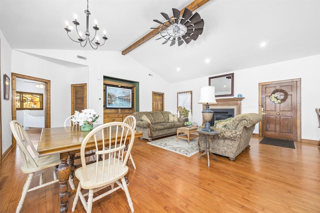 dining space featuring ceiling fan with notable chandelier, light wood-type flooring, and vaulted ceiling with beams