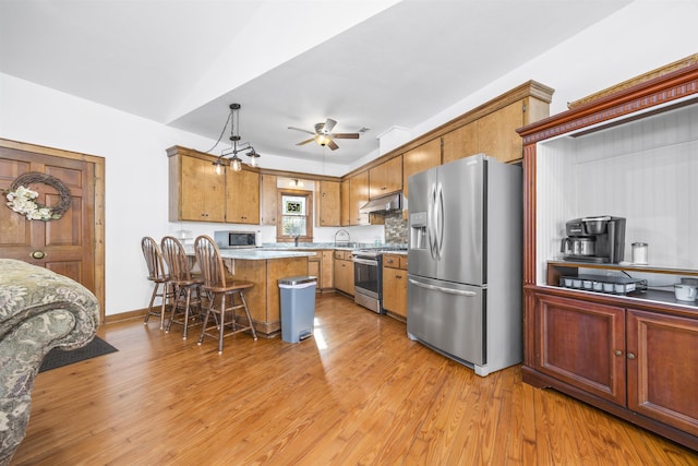 kitchen with appliances with stainless steel finishes, hanging light fixtures, backsplash, a kitchen breakfast bar, and light hardwood / wood-style floors