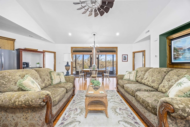 living room featuring ceiling fan with notable chandelier, light hardwood / wood-style floors, and vaulted ceiling