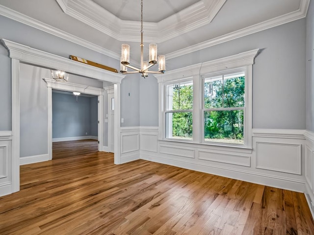 unfurnished dining area with hardwood / wood-style flooring, ornamental molding, a notable chandelier, and a tray ceiling