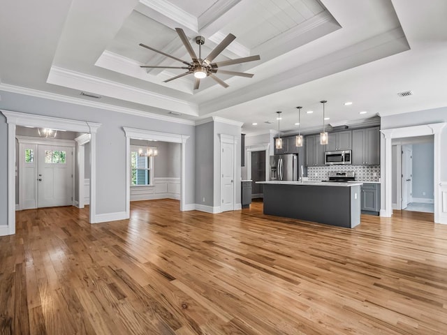 unfurnished living room featuring ceiling fan with notable chandelier, light hardwood / wood-style floors, and a raised ceiling