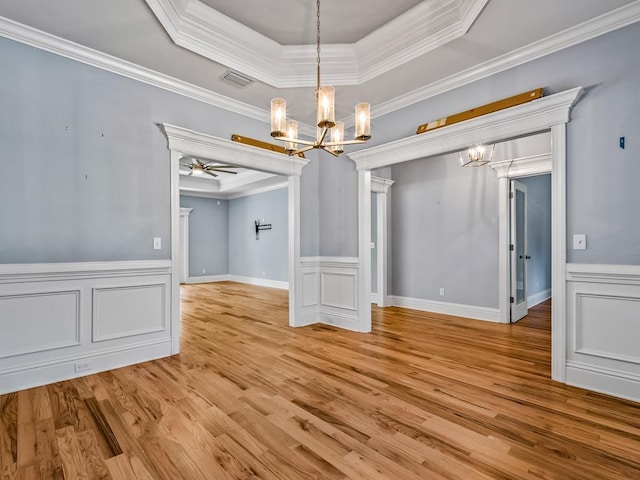 unfurnished dining area with crown molding, a raised ceiling, ceiling fan with notable chandelier, and light wood-type flooring