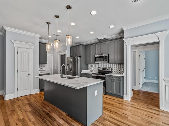 kitchen featuring gray cabinetry, decorative light fixtures, a center island with sink, stainless steel appliances, and light stone countertops