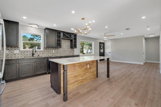 kitchen with decorative light fixtures, a kitchen island, decorative backsplash, sink, and light stone countertops