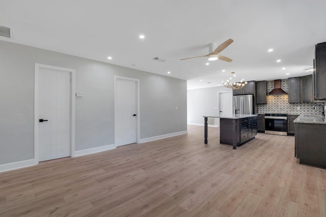 kitchen with light hardwood / wood-style floors, appliances with stainless steel finishes, backsplash, wall chimney range hood, and a kitchen island