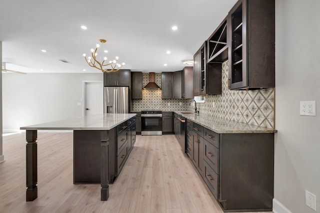 kitchen featuring a center island, wall chimney range hood, stainless steel appliances, sink, and hanging light fixtures