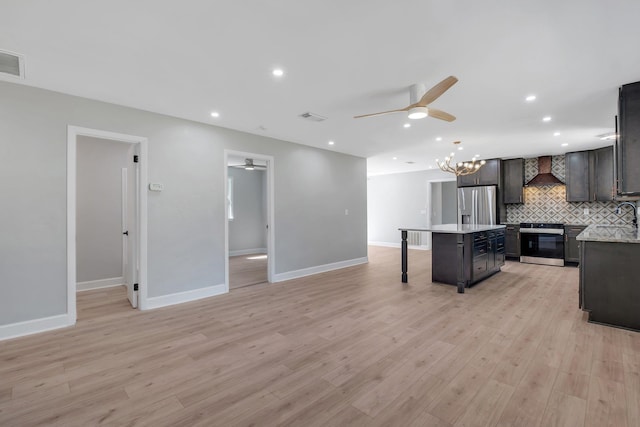 kitchen featuring appliances with stainless steel finishes, a kitchen island, wall chimney exhaust hood, and light hardwood / wood-style floors