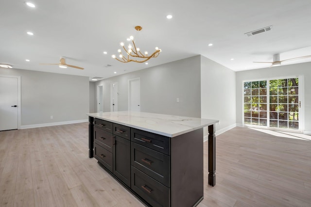 kitchen featuring light stone counters, decorative light fixtures, light hardwood / wood-style floors, and ceiling fan with notable chandelier