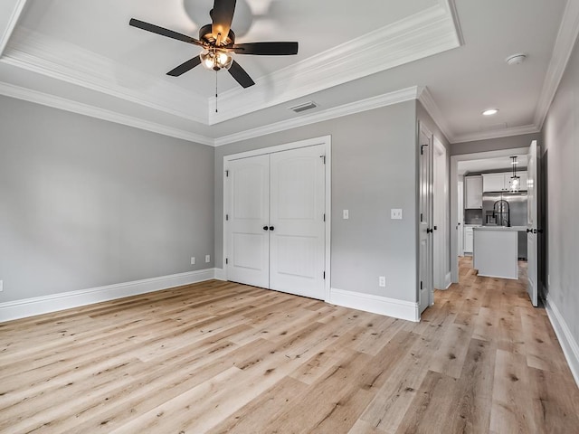 unfurnished bedroom featuring ornamental molding, ceiling fan, a tray ceiling, light wood-type flooring, and a closet