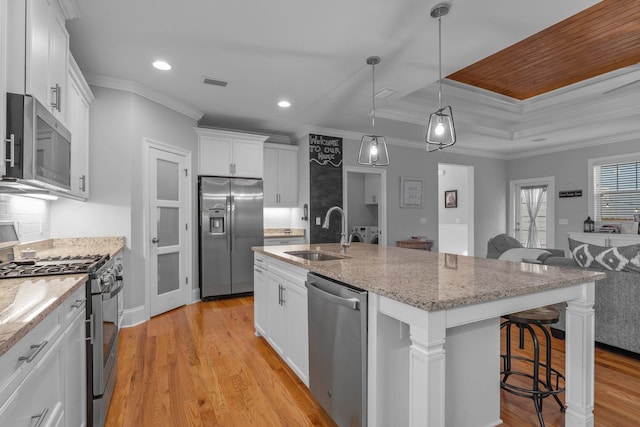 kitchen featuring sink, hanging light fixtures, stainless steel appliances, an island with sink, and white cabinets