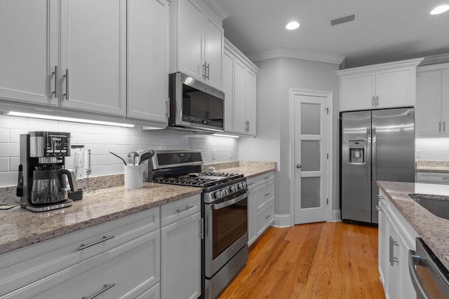 kitchen featuring white cabinetry, decorative backsplash, light stone counters, stainless steel appliances, and crown molding