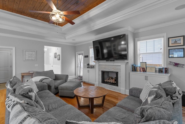 living room with wood ceiling, ornamental molding, a tray ceiling, a fireplace, and light hardwood / wood-style floors