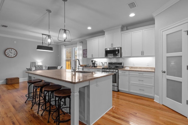 kitchen featuring an island with sink, appliances with stainless steel finishes, ornamental molding, and white cabinets