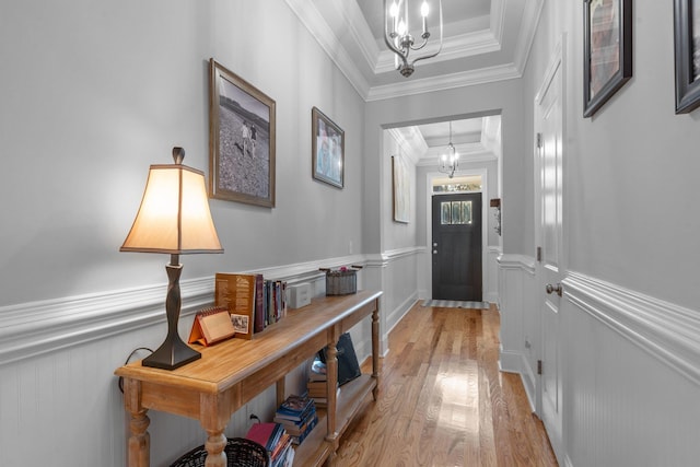 interior space with crown molding, a chandelier, a raised ceiling, and light hardwood / wood-style floors