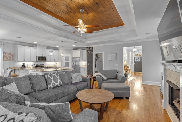 living room with sink, crown molding, light wood-type flooring, a raised ceiling, and ceiling fan