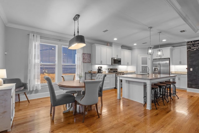 kitchen with pendant lighting, white cabinetry, stainless steel appliances, and a center island with sink