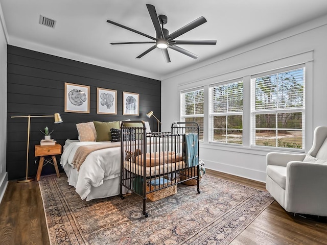 bedroom featuring ceiling fan, visible vents, wood finished floors, baseboards, and an accent wall