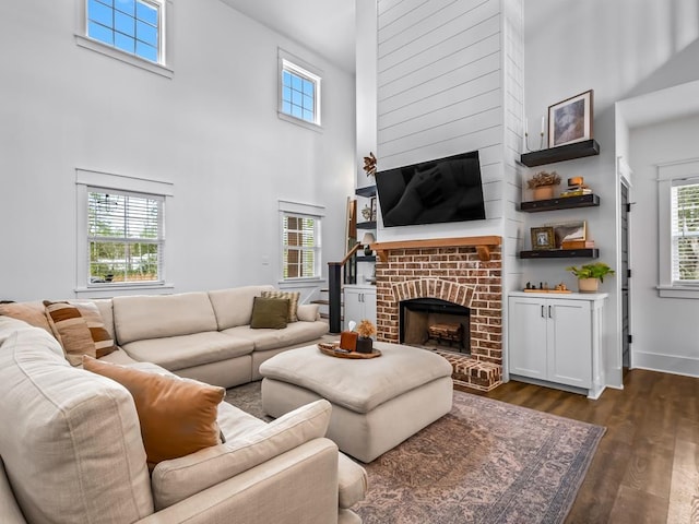 living area with dark wood-style flooring, a brick fireplace, a high ceiling, and a healthy amount of sunlight