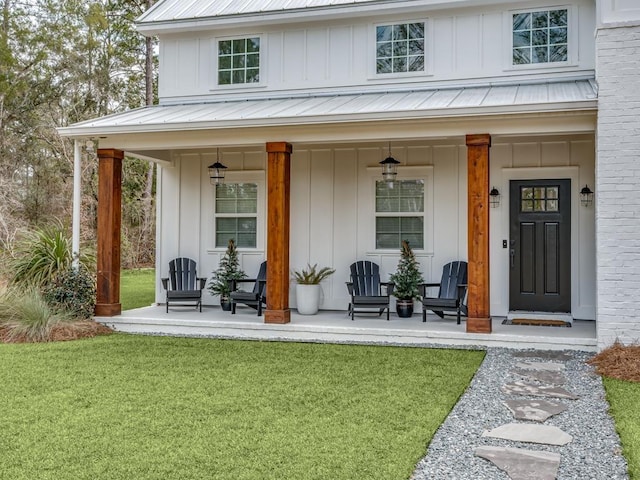 entrance to property with covered porch, board and batten siding, a yard, and metal roof
