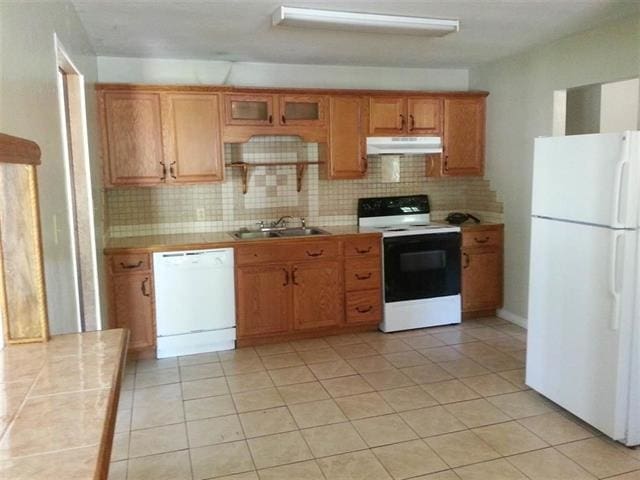 1411 California St, Tallahassee, FL 32304 - kitchen with white appliances, light tile patterned floors, under cabinet range hood, a sink, and backsplash