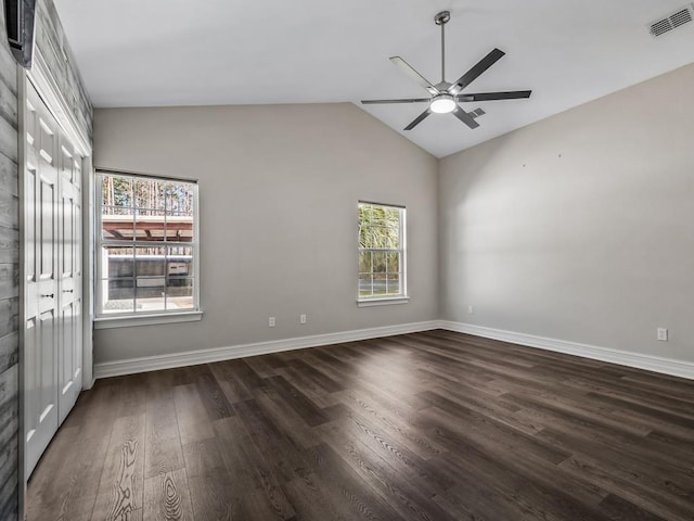 empty room featuring vaulted ceiling, dark wood-type flooring, visible vents, and baseboards