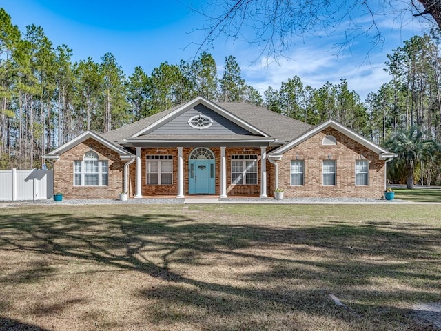 greek revival inspired property with covered porch, a front yard, fence, and brick siding