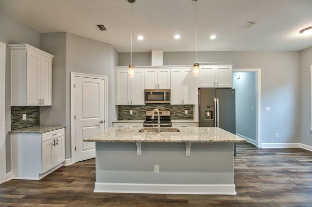 kitchen with white cabinetry, dark hardwood / wood-style floors, decorative light fixtures, a kitchen island with sink, and appliances with stainless steel finishes