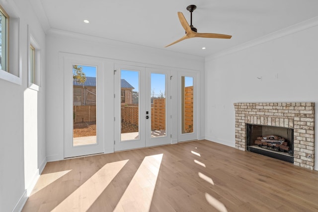 unfurnished living room featuring crown molding, ceiling fan, a fireplace, french doors, and light wood-type flooring