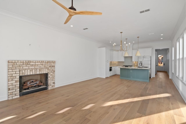 kitchen with stainless steel refrigerator with ice dispenser, crown molding, pendant lighting, a kitchen island with sink, and white cabinets