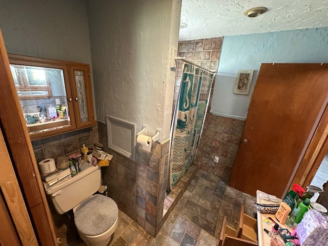 full bath with a textured wall, toilet, a stall shower, and tile walls