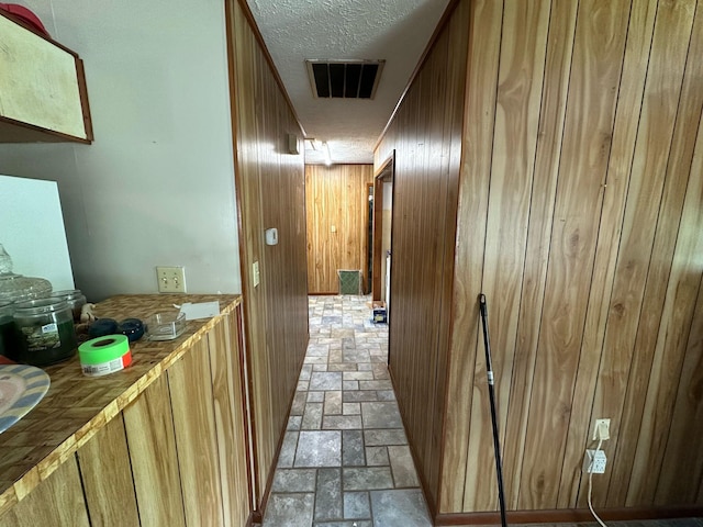 hallway featuring visible vents, stone finish flooring, a textured ceiling, and wood walls