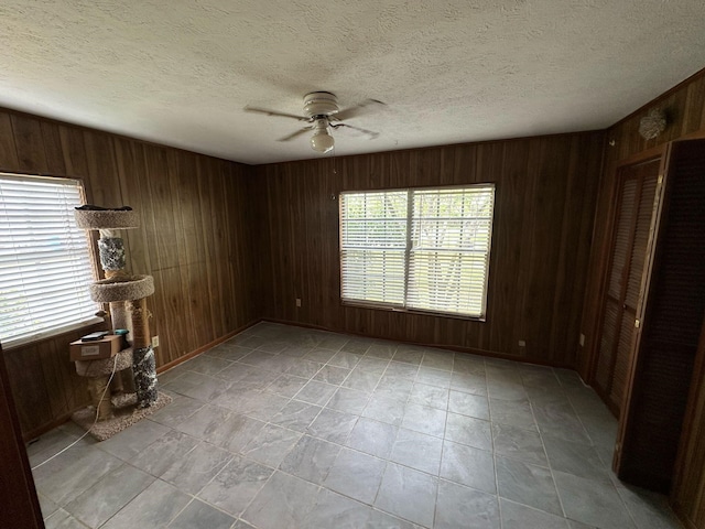 spare room with wood walls, a ceiling fan, and a textured ceiling