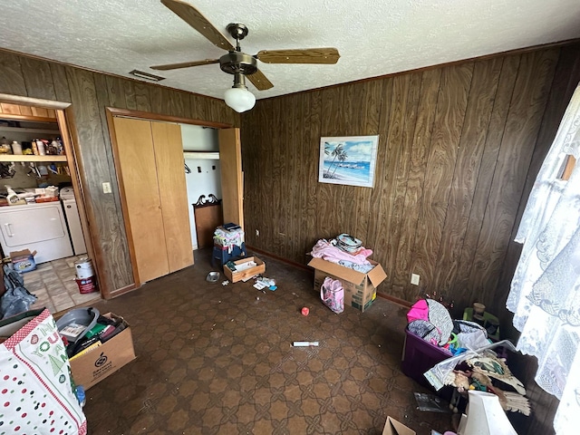 unfurnished bedroom with a textured ceiling, wood walls, visible vents, ceiling fan, and separate washer and dryer