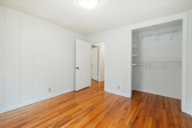 unfurnished bedroom featuring a spacious closet, baseboards, a closet, and wood finished floors