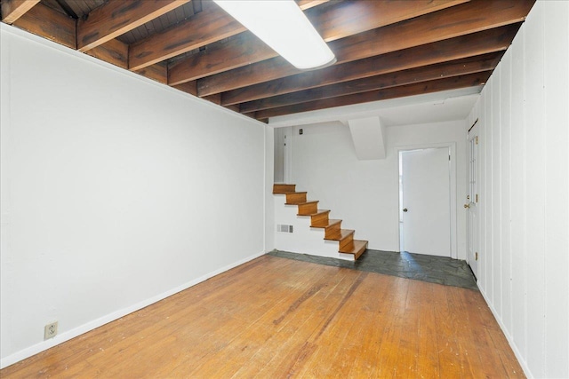 finished below grade area featuring wood-type flooring, visible vents, baseboards, and stairs