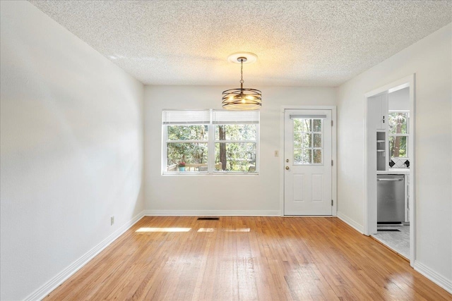 interior space with a textured ceiling, light wood-type flooring, visible vents, and baseboards