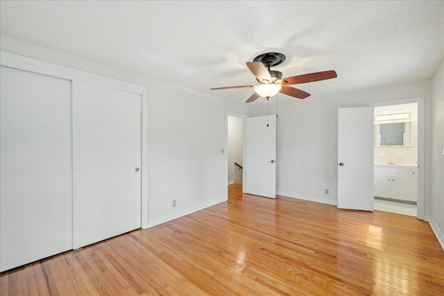 unfurnished bedroom featuring baseboards, ensuite bathroom, a textured ceiling, light wood-style floors, and a closet