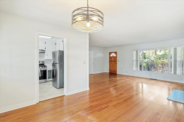 unfurnished living room featuring light wood-style flooring, a textured ceiling, baseboards, and a notable chandelier