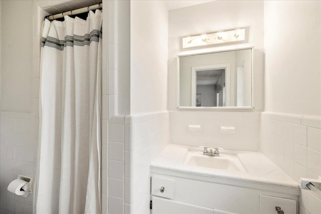 full bathroom featuring a wainscoted wall, curtained shower, tile walls, and vanity