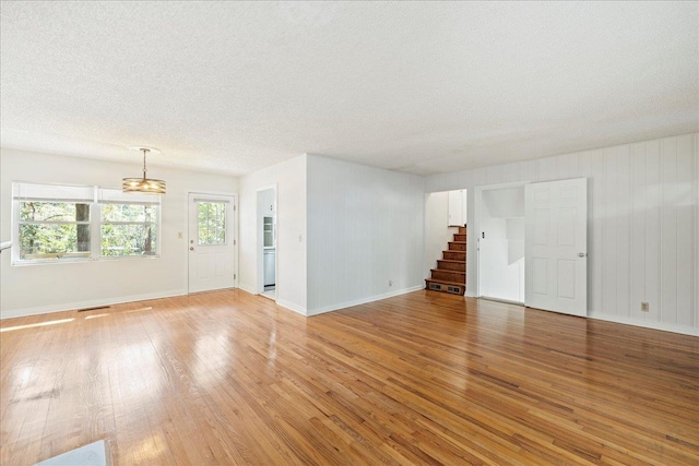 spare room with stairs, a textured ceiling, baseboards, and light wood-style floors