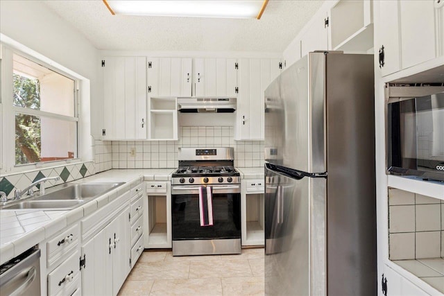 kitchen featuring white cabinets, tile countertops, appliances with stainless steel finishes, under cabinet range hood, and a sink