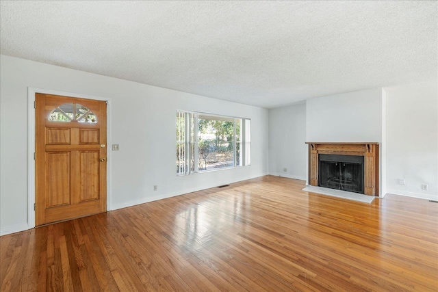 unfurnished living room with a textured ceiling, a fireplace, wood finished floors, and baseboards