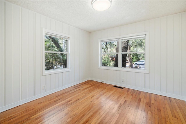 empty room featuring a textured ceiling, visible vents, and light wood-style floors