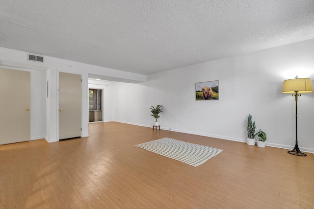 interior space featuring baseboards, visible vents, a textured ceiling, and light wood finished floors