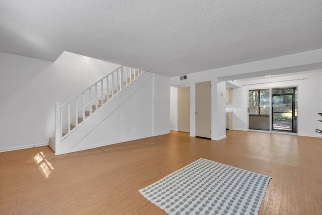 unfurnished living room featuring stairs, a textured ceiling, wood finished floors, and visible vents