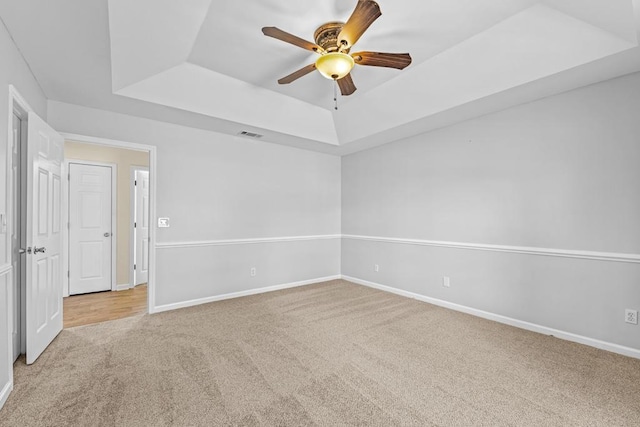 carpeted empty room with a raised ceiling and ceiling fan