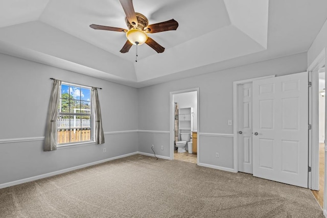 unfurnished bedroom with vaulted ceiling, connected bathroom, light carpet, and a tray ceiling