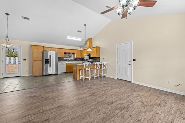 kitchen with stainless steel appliances, hanging light fixtures, backsplash, and a kitchen breakfast bar